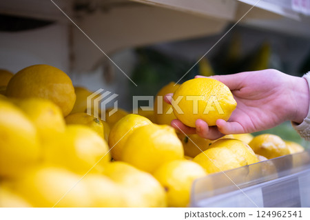 Shopper's hand holding a lemon in a supermarket 124962541