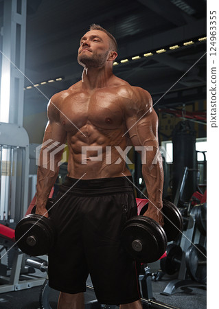 athletic man exercises in gym lifting heavy dumbbells while focusing on strength and endurance. environment is filled workout equipment and weights showcasing dedication fitness. athletic man exercises in gym lifting heavy dumbbells while focusing on strength and endurance. environment is filled workout equipment and weights showcasing dedication fitness. 124963355