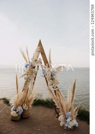 A wooden arch with pampas grass and flowers is on a cliff by the ocean A wooden arch with pampas grass and flowers is on a cliff by the ocean 124963766