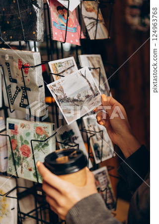 A person holds a coffee cup in front of a postcard display 124963768