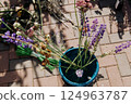 A blue pot with purple flowers sits on a brick floor 124963787