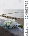 A bouquet of white flowers sits on a ledge by the ocean 124963792