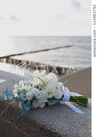 A bouquet of white flowers sits on a ledge by the ocean 124963792