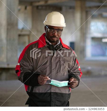 African american builder stands at construction site and holds medical mask 124963853