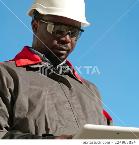 African american worker with tablet computer stands at construction site African american worker with tablet computer stands at construction site 124963854