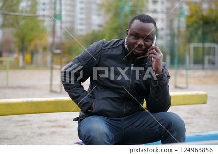 African american man sits at sport ground and speaks on smartphone 124963856