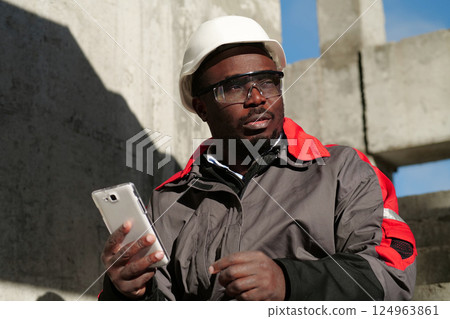 African american workman with smartphone at construction site African american workman with smartphone at construction site 124963861