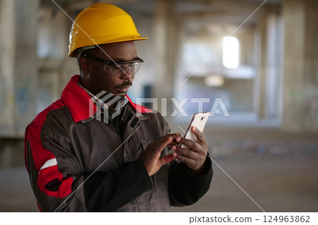 African american workman with smartphone at construction site African american workman with smartphone at construction site 124963862