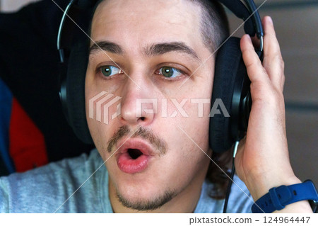 Enthusiastic conversation fills the air as a man wearing headphones interacts with friends during an intense gaming 124964447