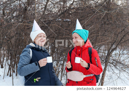 Friends celebrate winter together with warm drinks and party hats amidst a snowy landscape Friends celebrate winter together with warm drinks and party hats amidst a snowy landscape 124964627