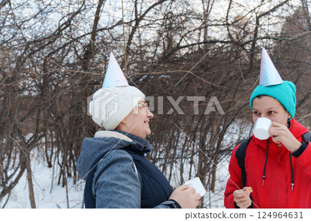 Friends savor the joy of winter in a snowy forest, wearing colorful party hats as they share warm drinks and snacks. Friends savor the joy of winter in a snowy forest, wearing colorful party hats as they share warm drinks and snacks. 124964631