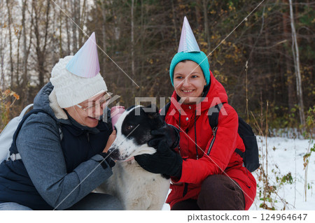 Two friends wearing colorful winter attire and party hats joyfully play in the snow Two friends wearing colorful winter attire and party hats joyfully play in the snow 124964647