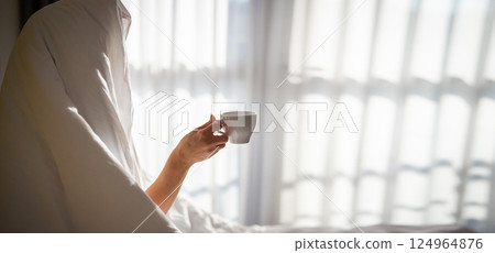 Woman with cup of coffee in the morning under the blanket at home Woman with cup of coffee in the morning under the blanket at home 124964876