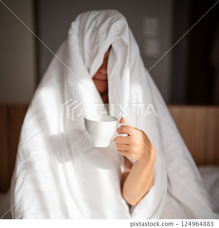 Woman with cup of coffee in the morning under the blanket at home 124964883