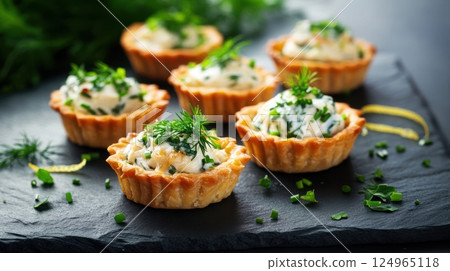 Golden tartlets filled with smoked mackerel mousse and topped with herbs, styled on slate with moody light and elegant textures. A refined and rustic savory appetizer scene. 124965118