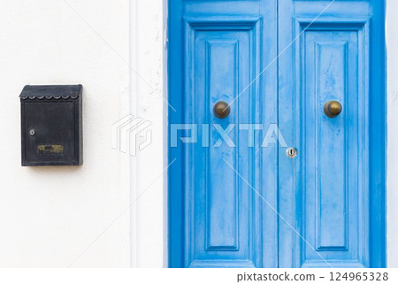 White wall with closed blue wooden doors and a black mail box White wall with closed blue wooden doors and a black mail box 124965328