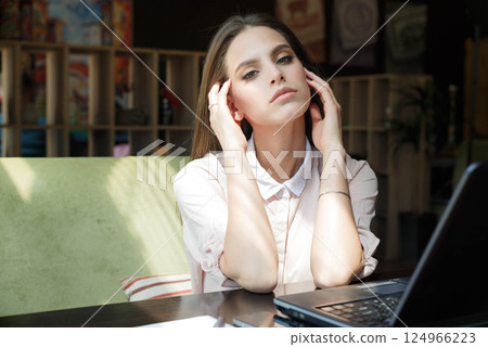 Beautiful girl at a table in a cafe is sitting in front of a laptop. Beautiful girl at a table in a cafe is sitting in front of a laptop. 124966223