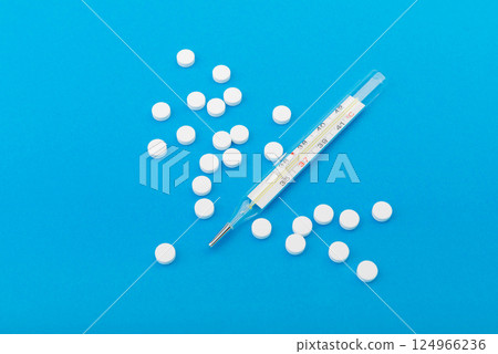 Glass thermometer between red pills and blue capsules 124966236