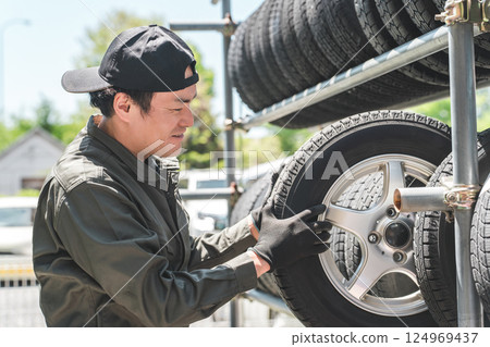 A male mechanic carrying studless tires from a tire rack A male mechanic carrying studless tires from a tire rack 124969437