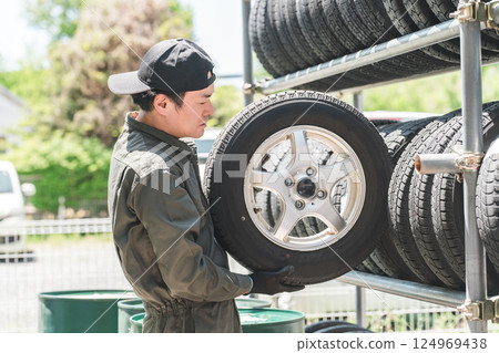 A male mechanic carrying studless tires from a tire rack A male mechanic carrying studless tires from a tire rack 124969438