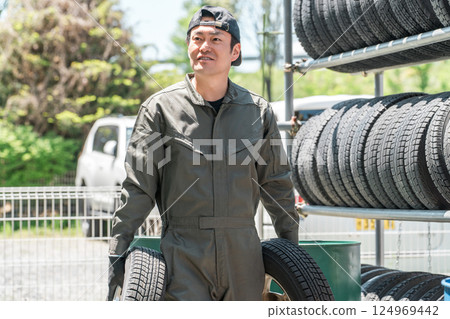 一名男性機械師從輪胎架上搬運鑲釘輪胎 一名男性機械師從輪胎架上搬運鑲釘輪胎 124969442