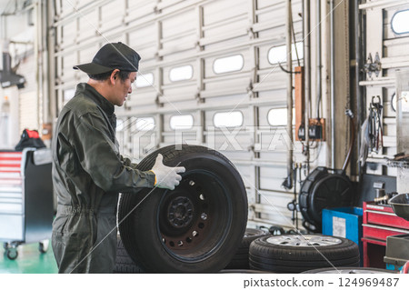Male mechanic carrying tires at an auto repair shop (physical labor, heavy work, heavy, back pain) 124969487