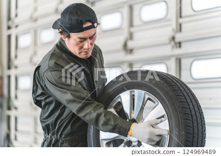 Male auto mechanic staff carrying tires at a repair shop Male auto mechanic staff carrying tires at a repair shop 124969489