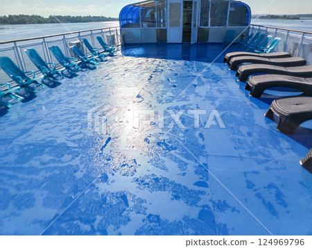 The morning sunlight reflected in droplets on the wet blue deck of the cruise ship, rows of sunbeds standing in a row The morning sunlight reflected in droplets on the wet blue deck of the cruise ship, rows of sunbeds standing in a row 124969796
