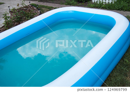 Close-up of an inflatable pool standing on the grass on a sunny summer day, the reflection of clouds on the surface of the water Close-up of an inflatable pool standing on the grass on a sunny summer day, the reflection of clouds on the surface of the water 124969799