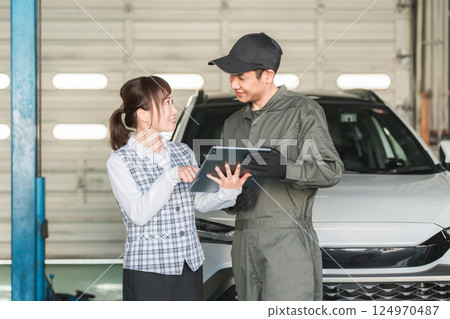 Male and female employees looking at a tablet in the pit of a maintenance workshop (automobile maintenance workshop, private vehicle inspection center, staff) 124970487