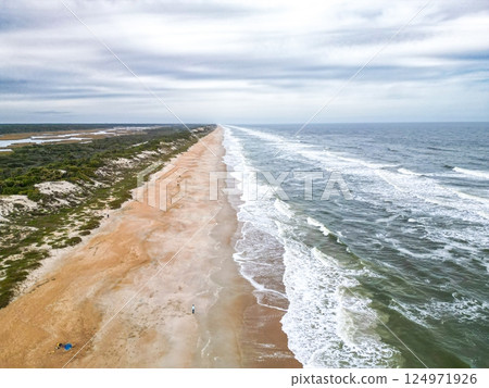 Wide Sandy Beach with Gentle Slope into Clear Blue-Green Ocean Under a Beautiful Sky and Dunes 124971926