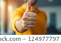 Person Giving Thumbs Up Gesture in Yellow Sweater with Blurred Background Expressing Positive 124977797