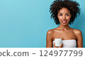 Young woman with curly hair holding skincare jar against a blue background, promoting beauty 124977799