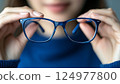 Young Woman Holding Glasses with Blue Frame, Close-Up View, Indoor Setting, Focus on Eyewear 124977800