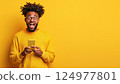 Excited young man holding smartphone on bright yellow background expressing happiness and surprise 124977801