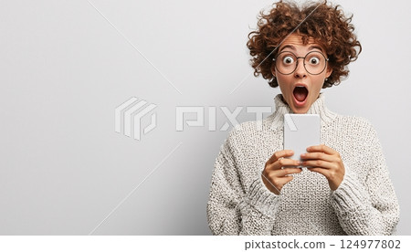 Surprised woman with curly hair checking smartphone and expressing excitement in casua Surprised woman with curly hair checking smartphone and expressing excitement in casua 124977802