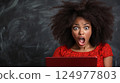 Shocked woman with curly hair expressing surprise while looking at laptop 124977803