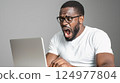 Shocked man with glasses reacting to unexpected news while using a laptop in a minimalistic  124977804