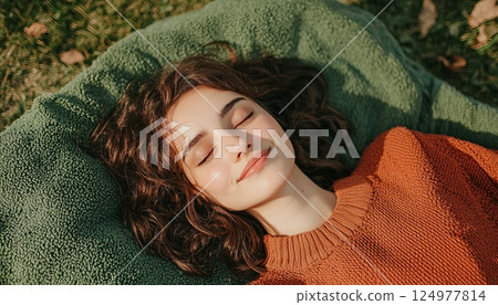 Young woman lounging in the sun on a green blanket, enjoying a peaceful moment in nature 124977814