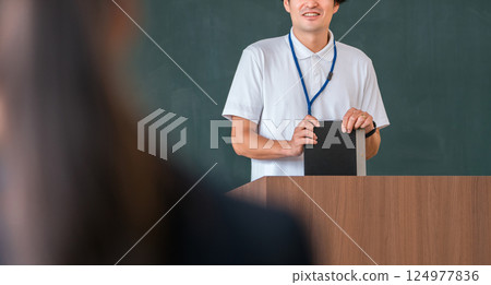 A male teacher teaching in front of a blackboard in a classroom 124977836