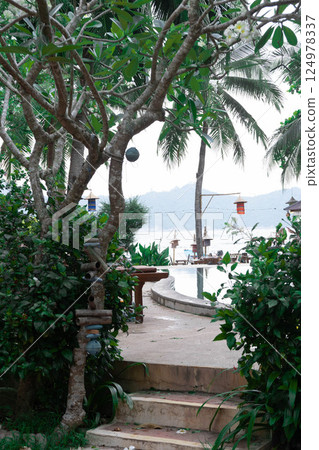 Lush greenery flanks a pathway leading directly to serene waters and palm trees.Thailand, Koh Phangan. 124978337