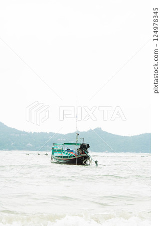 A humble fishing boat rests gently on the calm waters under a serene sky, surrounded by lush hills. 124978345