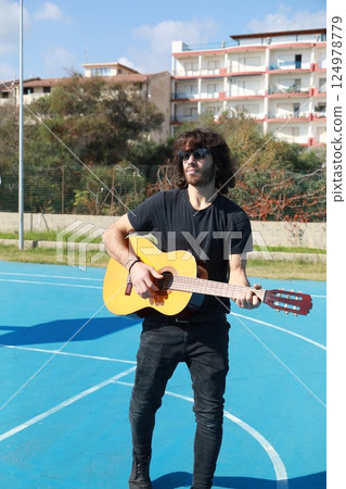 Long Hair Man Plays Classical Guitar Unleashed Outside In Blue Field Long Hair Man Plays Classical Guitar Unleashed Outside In Blue Field 124978779