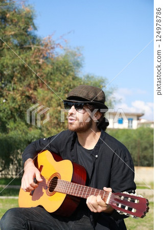 Male Street Artist Enjoys Playing Classical Guitar In A City Park 124978786
