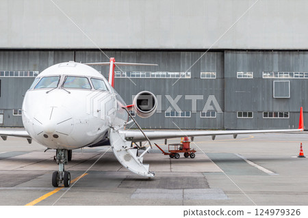 Regional aircraft with an opened gangway door at the airport near airplane hangar 124979326