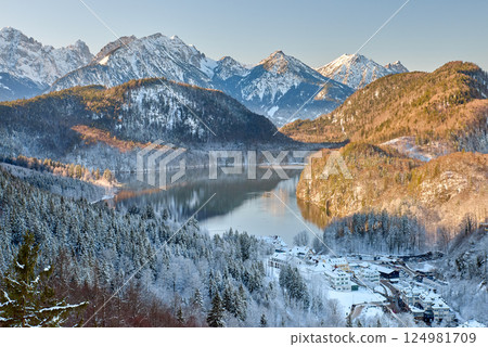 Snowy Mountain Landscape with Iconic Castle Overlooking Serene Lake and Alpine Peaks in Ethereal Winter Wonderland Bathed in Soft Dawn Light Snowy Mountain Landscape with Iconic Castle Overlooking Serene Lake and Alpine Peaks in Ethereal Winter Wonderland Bathed in Soft Dawn Light 124981709
