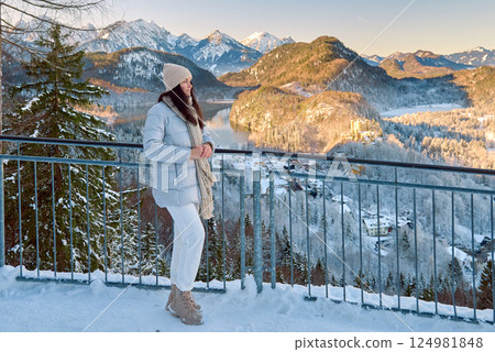 Enchanting Alpine Beauty Gazes at Majestic Neuschwanstein Castle Stunning Young Woman in White Winter Coat Admires Breathtaking Bavarian Mountain Landscape from Scenic Balcony 124981848