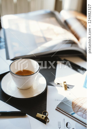 Coffee and Open Magazine on Desk in Sunlight 124982327