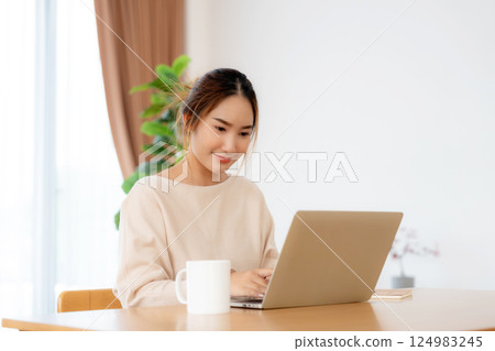 Happy young Asian woman working on laptop in living room 124983245