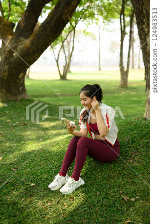 Smiling woman taking a break after workout using her smartphone with wireless earbuds 124983513